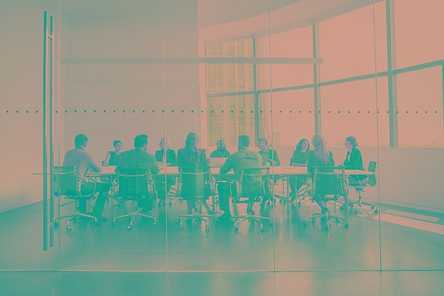 Mehrere Menschen sitzen um einen großen Tisch in einem Raum mit transparenten Wänden