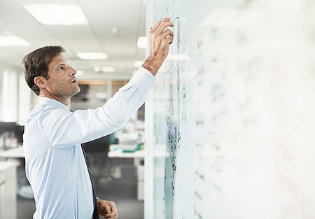 Ein Mann in weißem Hemd schreibt etwas mit einem Stift auf ein großes Whiteboard